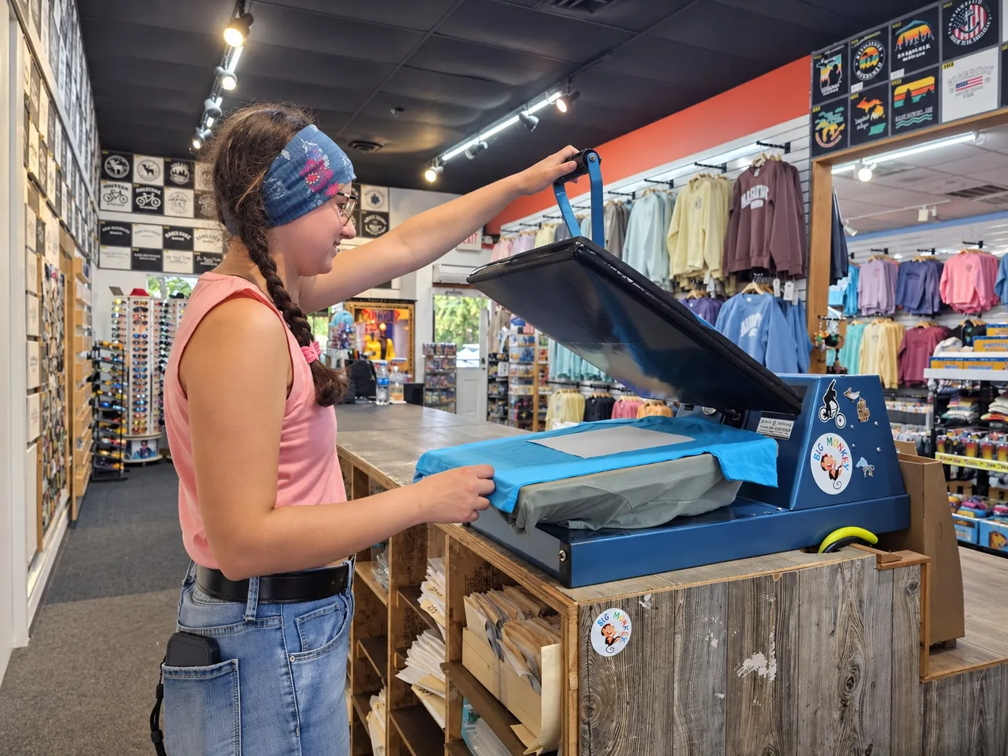 A Big Monkey staff member lifting the lid of the blue heat press over a blue t-shirt on the counter